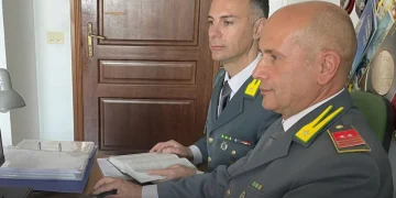 Militari Guardia di Finanza in divisa lavorano al computer e sui documenti
