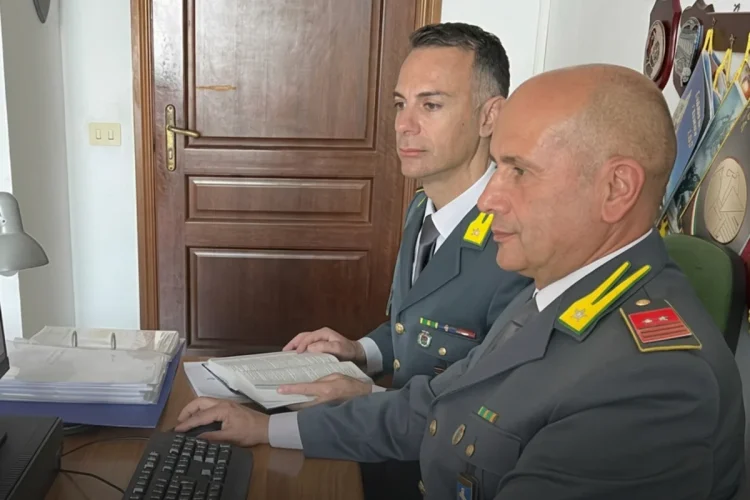 Militari Guardia di Finanza in divisa lavorano al computer e sui documenti
