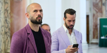 Andrew Tate con giacca viola guarda avanti con Tristan Tate al telefono. Fratelli Tate, custodia cautelare confermata a Miami: si oppongono all'estradizione nel Regno Unito