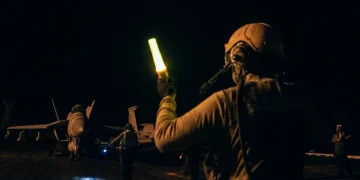 Un marinaio guida un aereo da caccia F/A-18 sulla portaerei di notte.