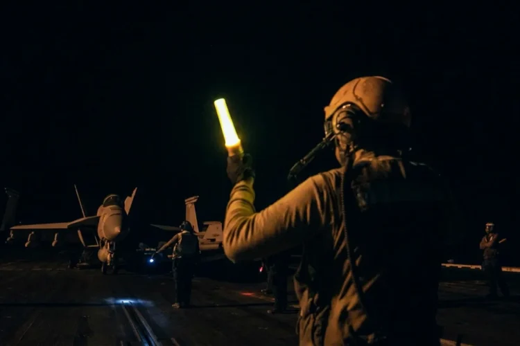 Un marinaio guida un aereo da caccia F/A-18 sulla portaerei di notte.