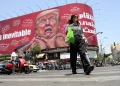 Donna iraniana cammina, tabellone anti-USA con Trump in strada a Tehran.