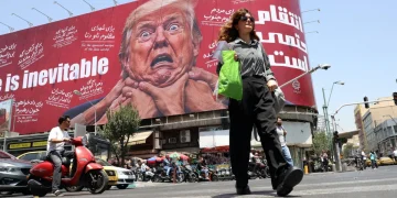 Donna iraniana cammina, tabellone anti-USA con Trump in strada a Tehran.
