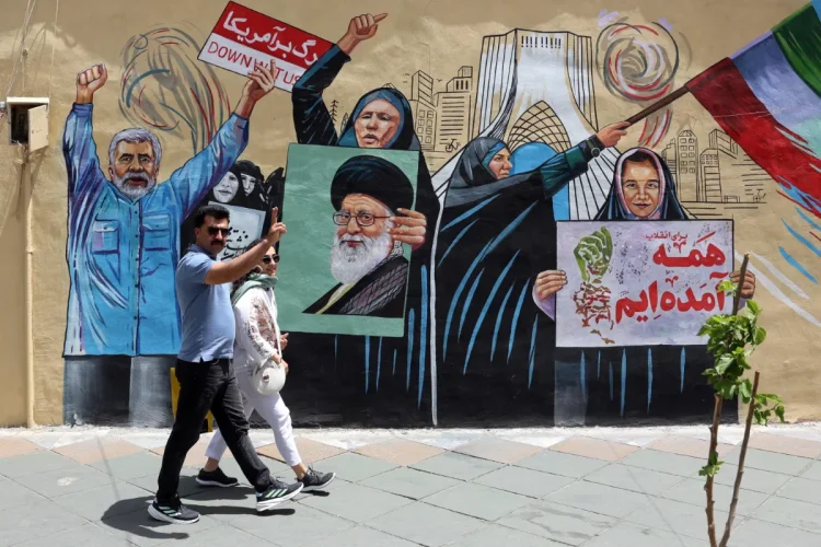 an-iranian-couple-walks-next-to-a-anti-us-and-israel-mural-in-a-street-in-tehran-1200x800.webp