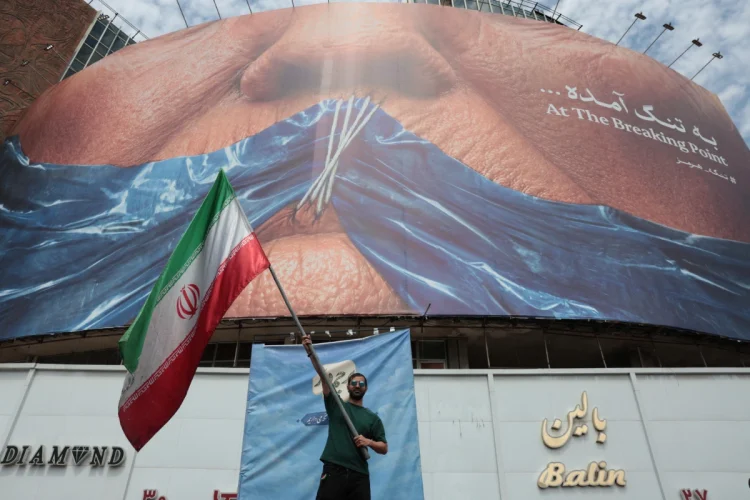 an-iranian-man-holds-iran-s-national-flag-in-front-of-a-huge-anti-us-billboard-r-1200x800.webp