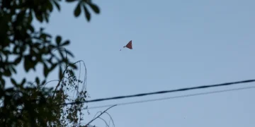 Un piccolo drone rosso vola solitario nel cielo azzurro.