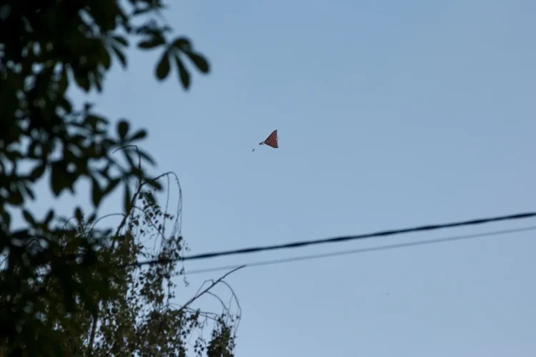 Un piccolo drone rosso vola solitario nel cielo azzurro.