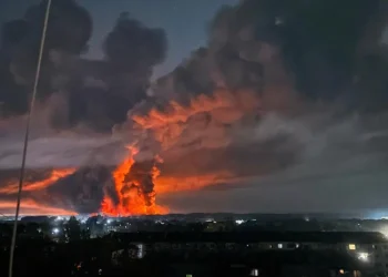 Vasto incendio notturno con fiamme rosse e fumo denso sopra città