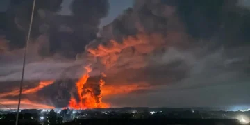 Vasto incendio notturno con fiamme rosse e fumo denso sopra città