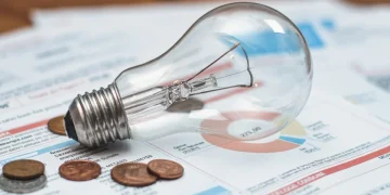 Lampadina, monete e bolletta energetica su tavolo di legno