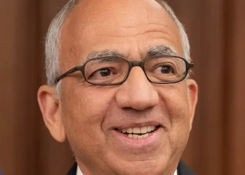 Carlos Cordeiro sorride, indossa occhiali e spilla FIFA/USA sulla giacca.