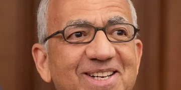 Carlos Cordeiro sorride, indossa occhiali e spilla FIFA/USA sulla giacca.