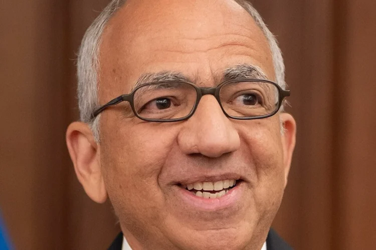 Carlos Cordeiro sorride, indossa occhiali e spilla FIFA/USA sulla giacca.