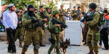 Soldati israeliani pattugliano strada con un colono ebreo ortodosso.