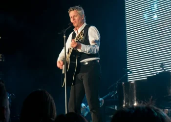 Cantante biondo suona chitarra acustica e canta sul palco illuminato
