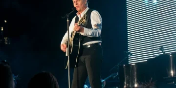 Cantante biondo suona chitarra acustica e canta sul palco illuminato