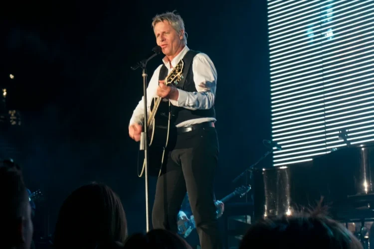Cantante biondo suona chitarra acustica e canta sul palco illuminato