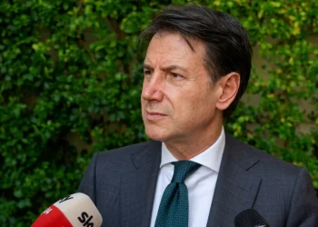 Giuseppe Conte parla ai microfoni con sfondo di verde.