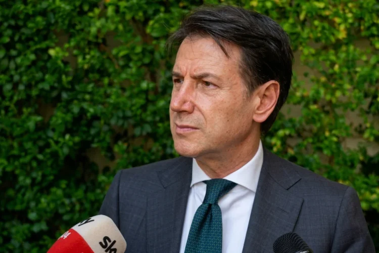 Giuseppe Conte parla ai microfoni con sfondo di verde.