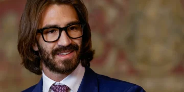 Leonardo Del Vecchio Jr. sorride indossando occhiali neri e giacca blu.