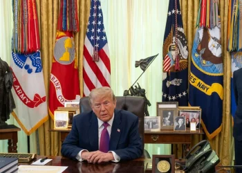 Donald Trump siede alla scrivania nell'Ufficio Ovale con un assistente.