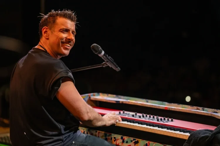 Francesco Gabbani sorride e suona la tastiera durante un concerto.
