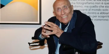 Franco Fontana, anziano, sorride in primo piano con occhiali.