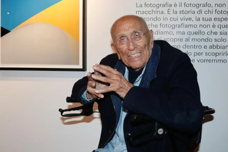 Franco Fontana, anziano, sorride in primo piano con occhiali.
