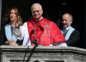 Cardinale sorridente saluta da balcone con collaboratori a San Marino