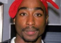 Tupac Shakur con bandana rossa, piercing al naso, collana d'oro.