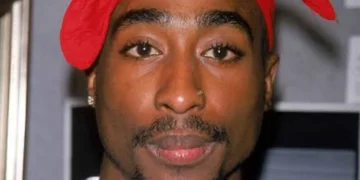 Tupac Shakur con bandana rossa, piercing al naso, collana d'oro.