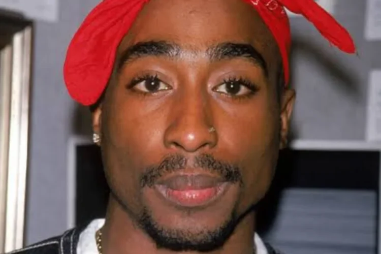 Tupac Shakur con bandana rossa, piercing al naso, collana d'oro.