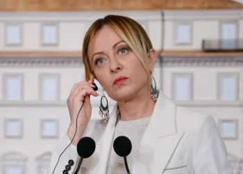 Giorgia Meloni con auricolare parla al microfono in un evento pubblico