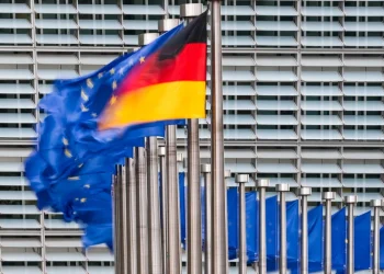 Bandiera della Germania e bandiere UE sventolano davanti a edificio moderno.