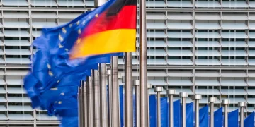 Bandiera della Germania e bandiere UE sventolano davanti a edificio moderno.