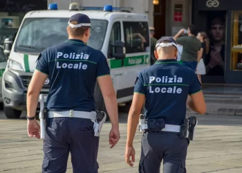 Due agenti di Polizia Locale camminano per strada, vicino a veicolo