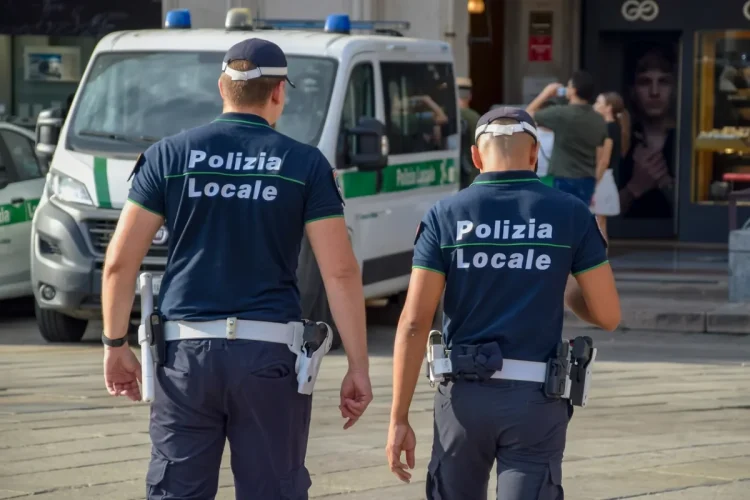Due agenti di Polizia Locale camminano per strada, vicino a veicolo