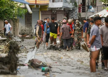 Persone in strada fangosa con bufalo morto dopo alluvione Nepal