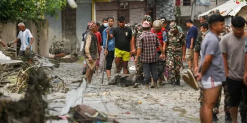Persone in strada fangosa con bufalo morto dopo alluvione Nepal