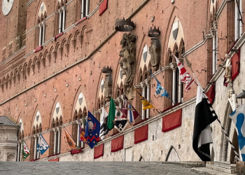 Palazzo Pubblico a Siena adornato con le bandiere delle Contrade del Palio. Palio di Siena, nuovo rinvio per la pioggia: esposta la bandiera verde