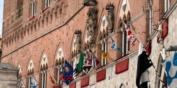 Palazzo Pubblico a Siena adornato con le bandiere delle Contrade del Palio. Palio di Siena, nuovo rinvio per la pioggia: esposta la bandiera verde
