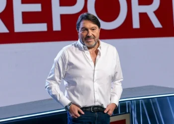 Sigfrido Ranucci sorride in studio con logo Report rosso.
