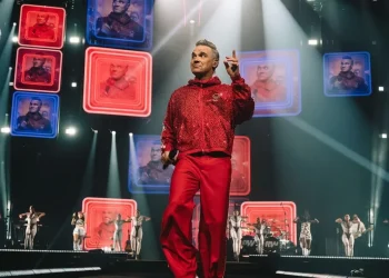 Robbie Williams indossa tuta rossa sul palco di un concerto