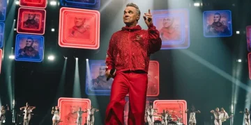 Robbie Williams indossa tuta rossa sul palco di un concerto