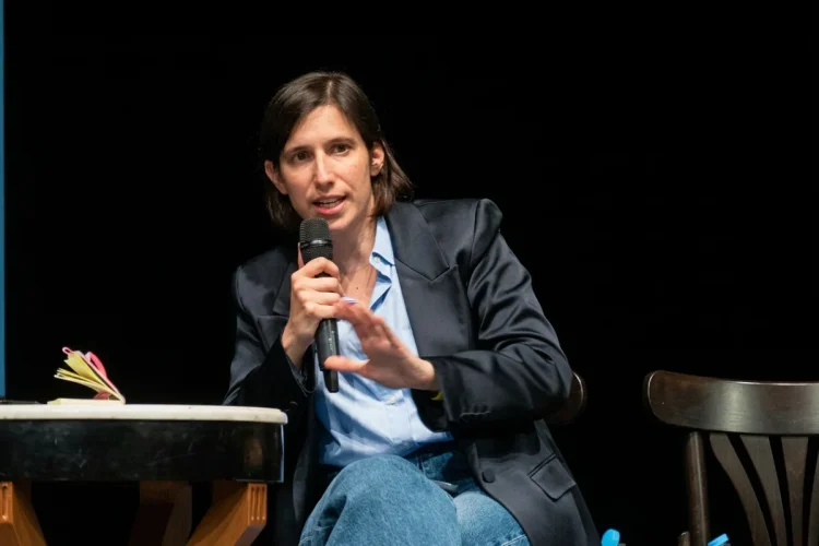 Elly Schlein parla al microfono gesticolando, indossa giacca scura.