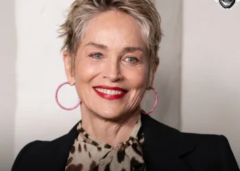Sharon Stone sorride con orecchini rosa, capelli corti e giacca scura.