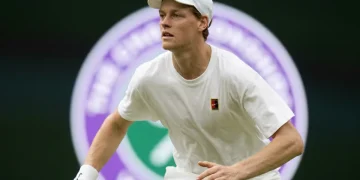 Jannik Sinner in campo con abbigliamento bianco, tiene racchetta.