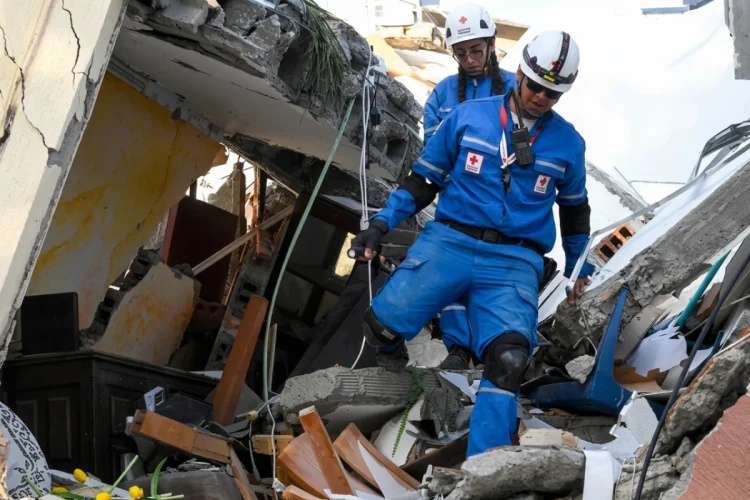 Soccorritori della Croce Rossa camminano tra le macerie di un edificio crollato