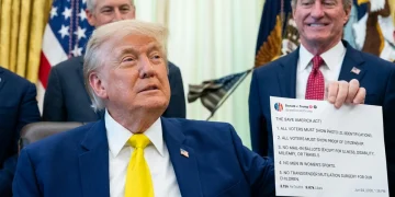 Donald Trump con giacca blu e cravatta gialla in un ufficio.