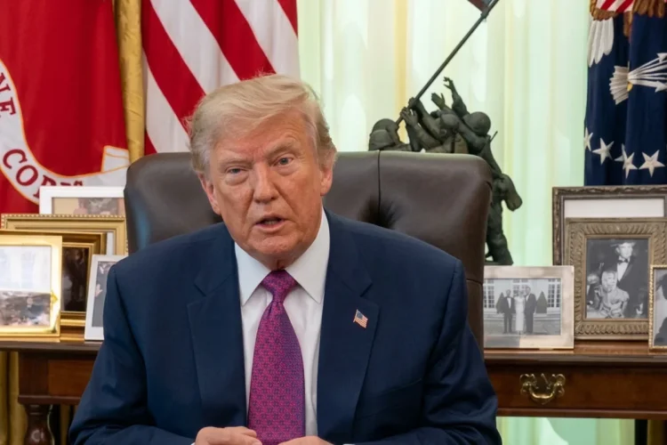 Donald Trump parla in giacca e cravatta davanti a bandiere americane.